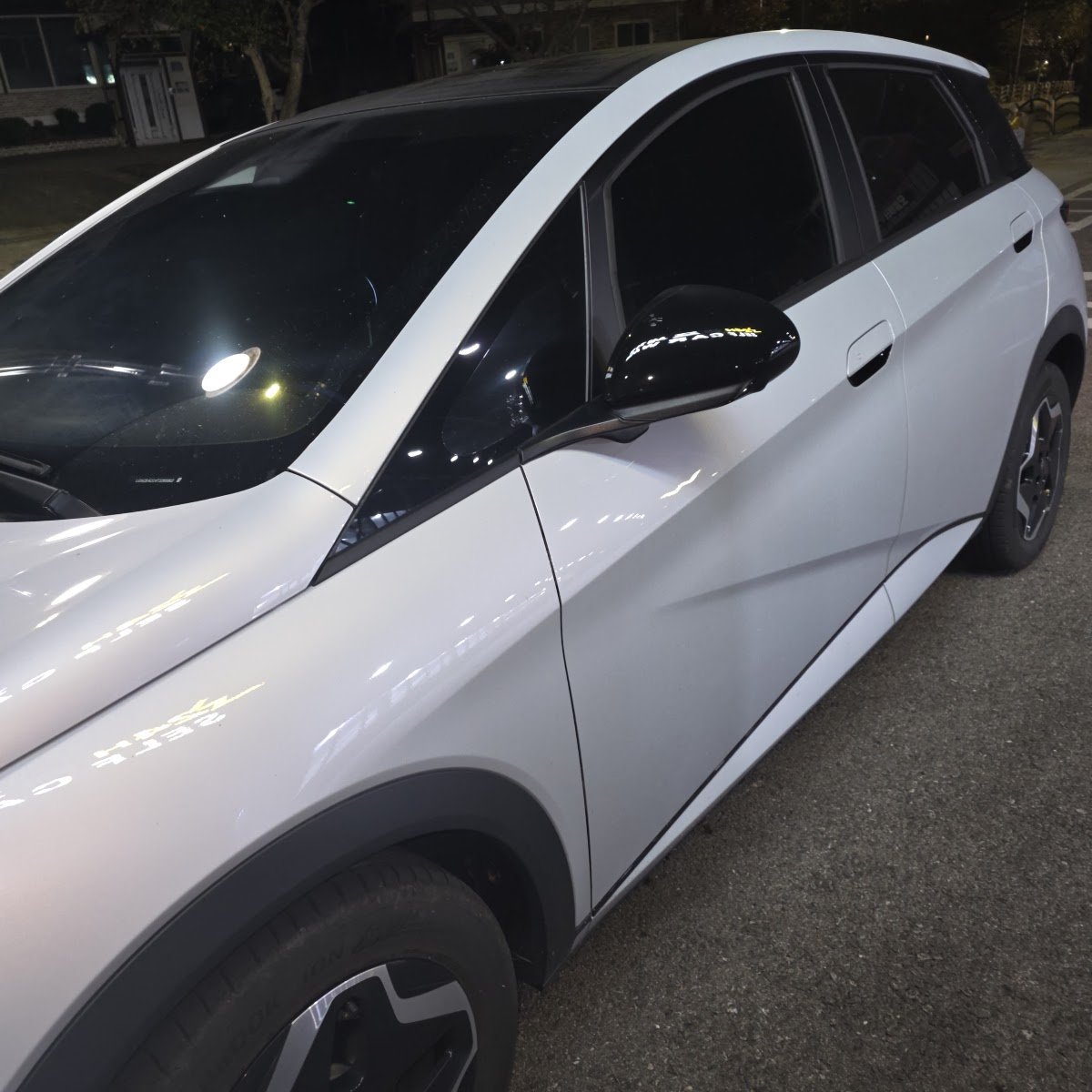 밤에 주차장에 세워 둔 흰색 BYD 돌핀의 앞문과 옆모습